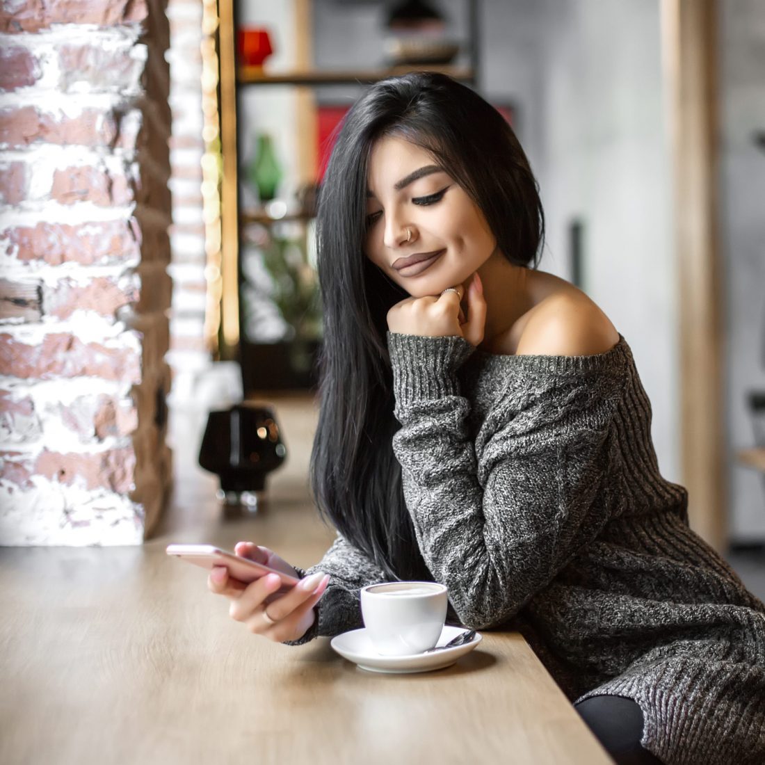Beautiful girl uses a phone and drinks coffee, sitting in a cozy